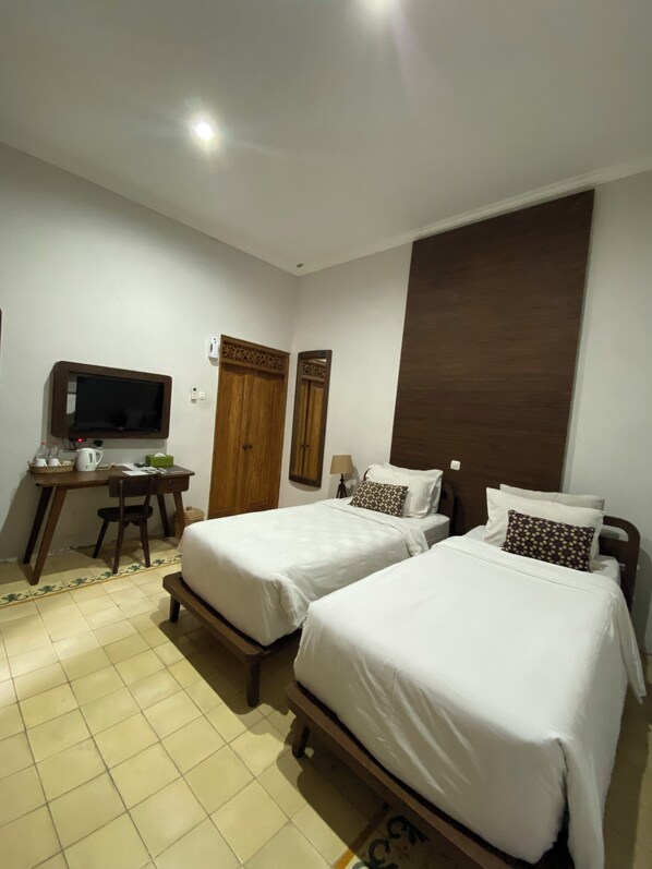 Habitación de hotel con dos camas, un escritorio con televisor, una silla y una mesita con tetera y tazas.