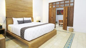 Quarto com cama de madeira, roupa de cama branca, mesa de cabeceira, abajur e guarda-roupa de madeira com portas de vidro.