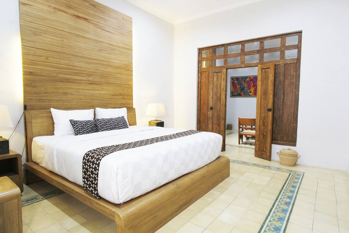 Une chambre à coucher avec un lit en bois, du linge de lit blanc, une table de chevet, une lampe et une armoire en bois dotée de portes en verre.