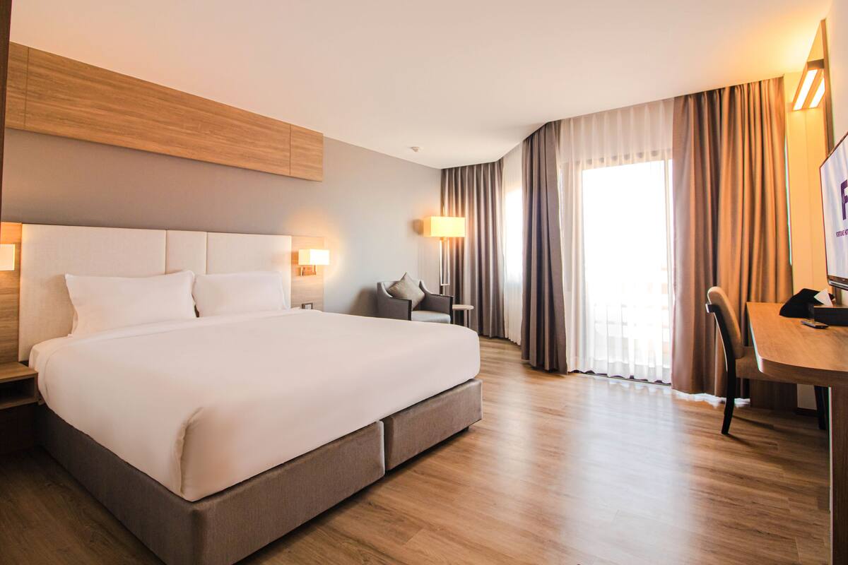 A hotel room with a large bed, bedside tables, a desk with a chair, a lamp, and a TV.