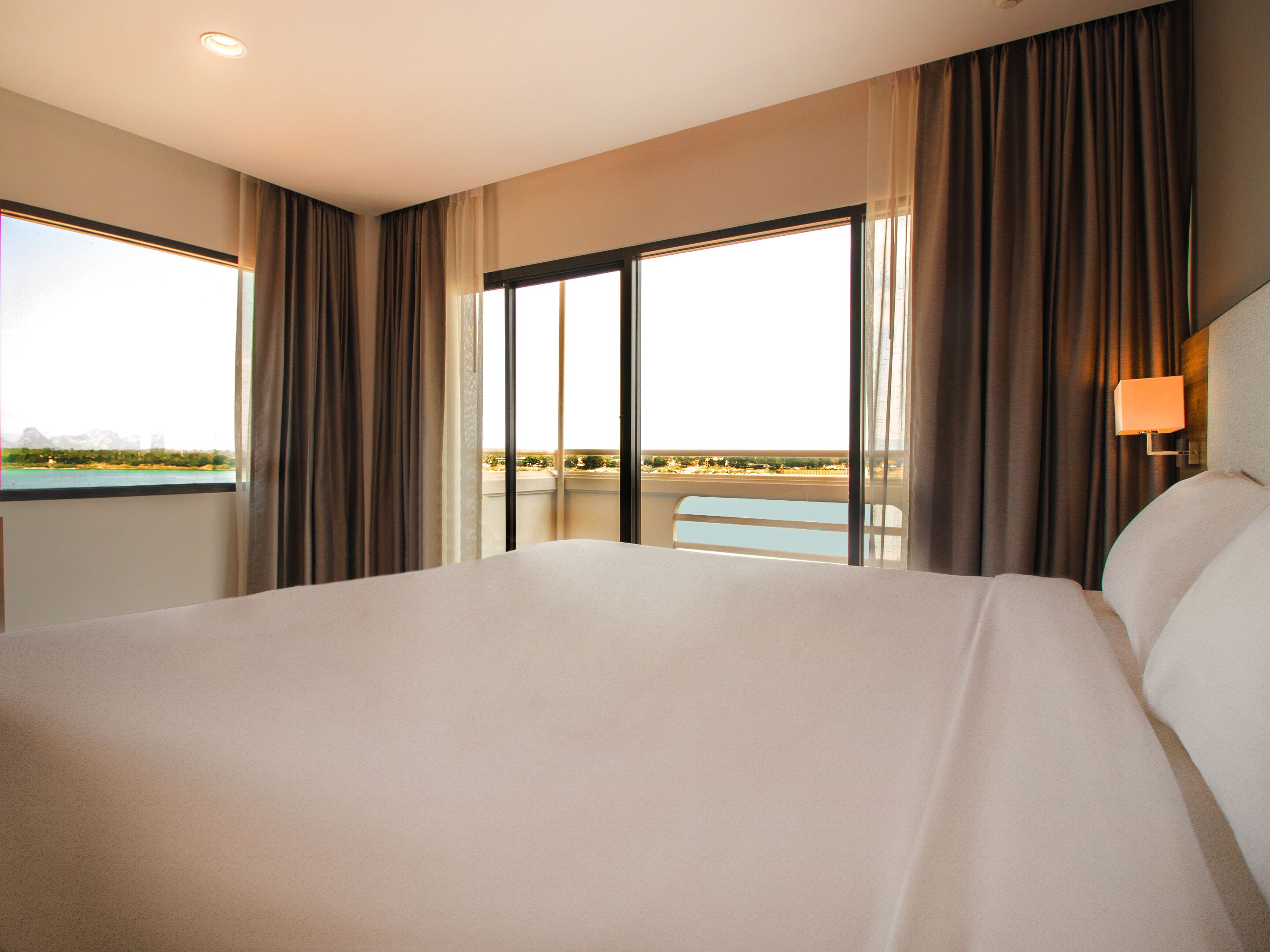 A large bed in a hotel room with a view of a cityscape through a large window.