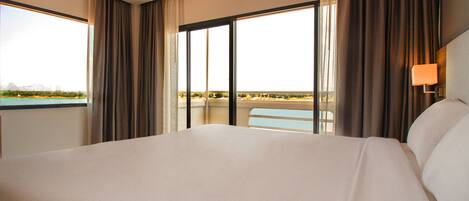A large bed in a hotel room with a view of a cityscape through a large window.