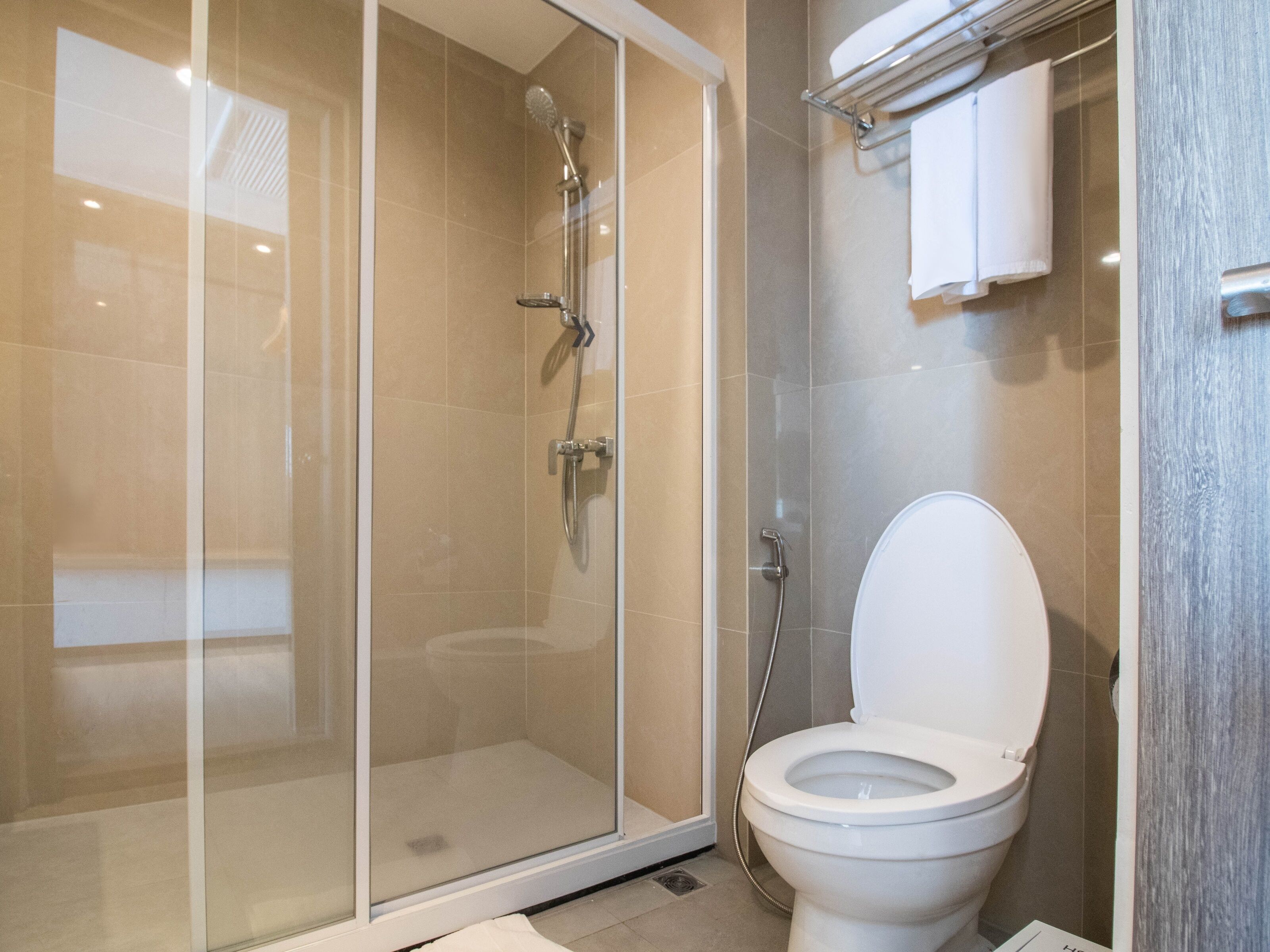 Een moderne badkamer met een douchecabine van glas, een wit toilet en een handdoekrek.