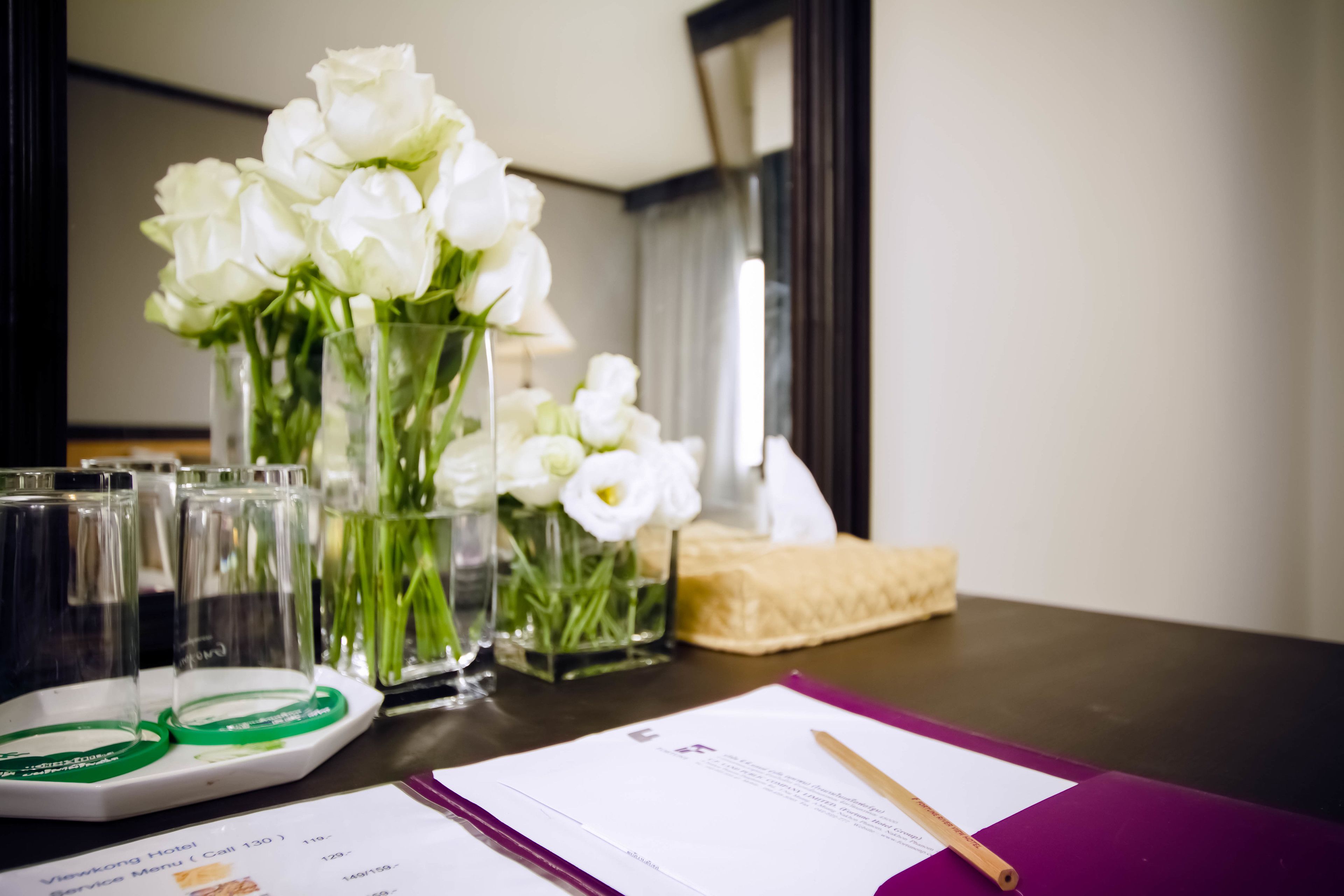 A table with a menu, a notepad, a pen, and a vase with white flowers.