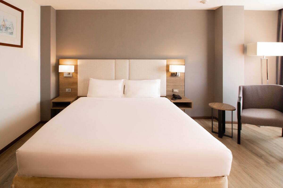 A hotel room with a large bed, two bedside tables with lamps, a chair, and a small table.