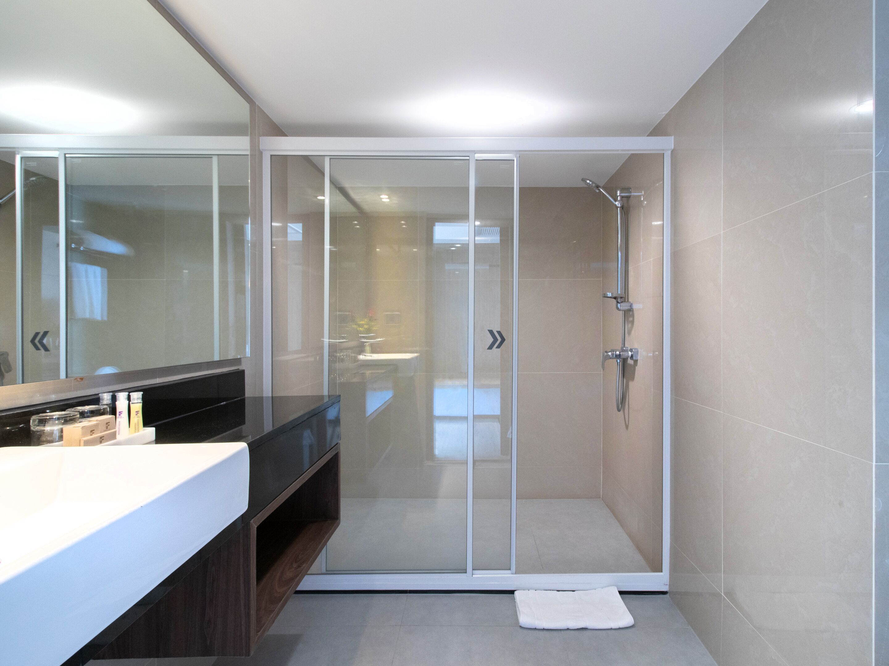 A modern bathroom with a glass-enclosed shower, a large mirror, and a vanity with toiletries.