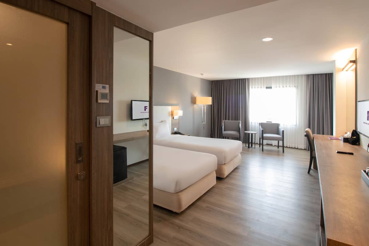 A hotel room with two beds, a desk, a chair, a TV, and a window with curtains.