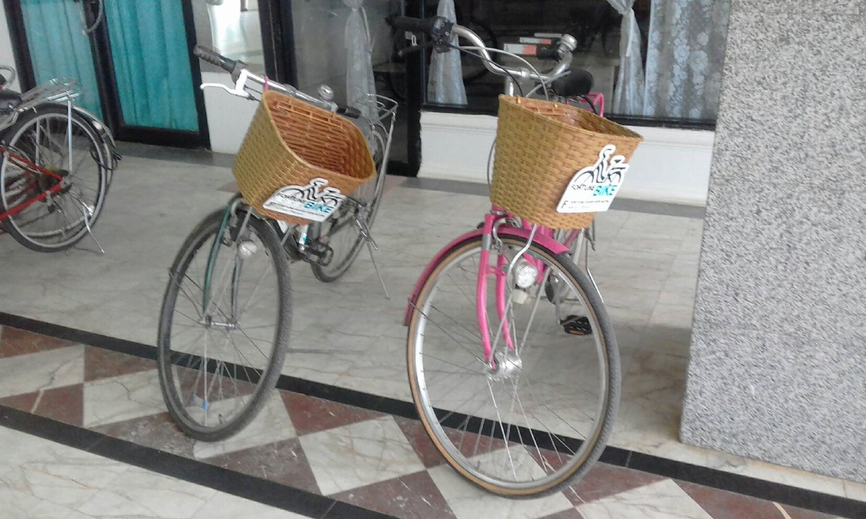 Two bicycles with wicker baskets, parked indoors on a tiled floor.