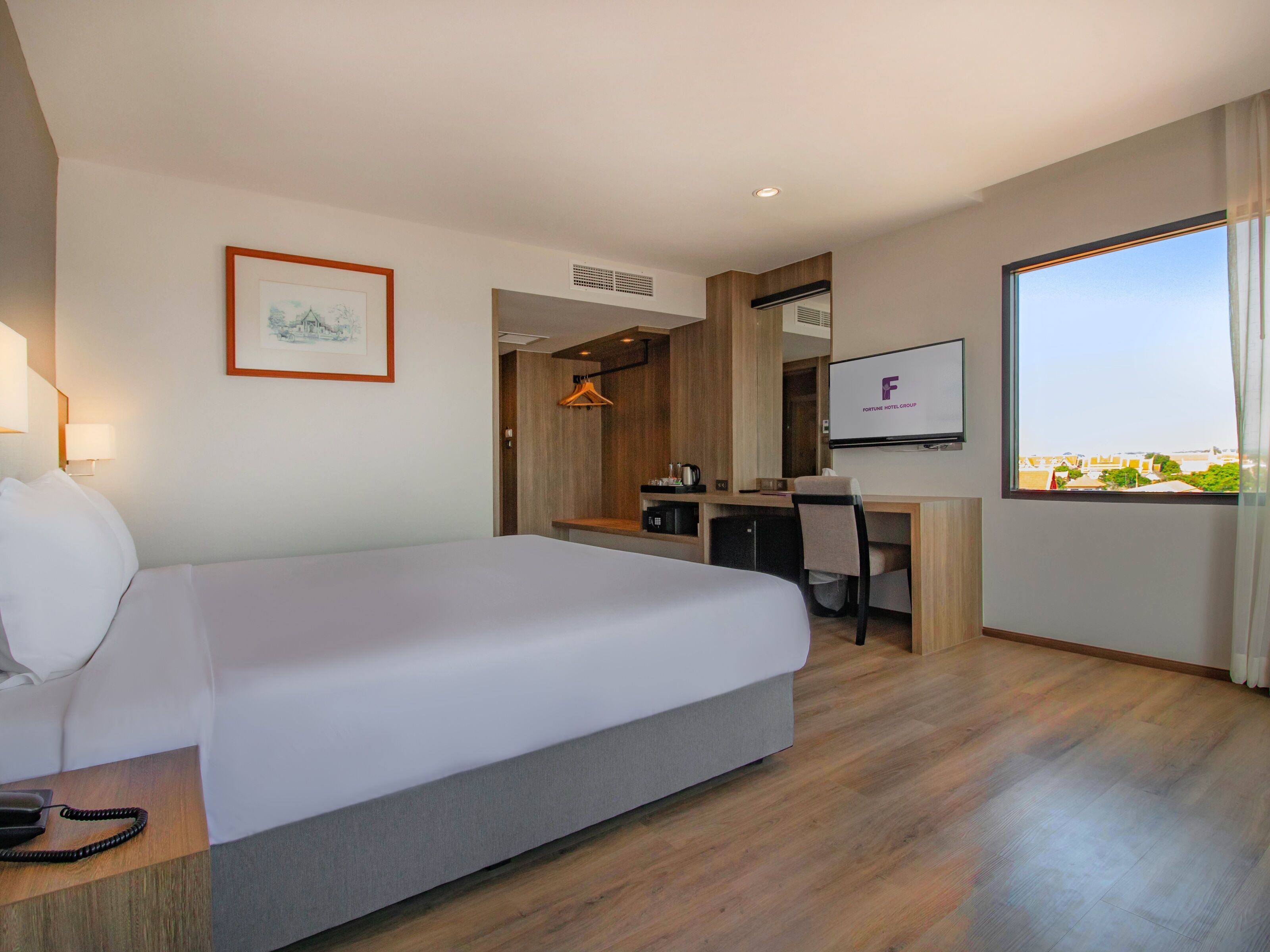 Une chambre d’hôtel avec un lit, un bureau, une chaise, une télévision et un tableau encadré au mur.