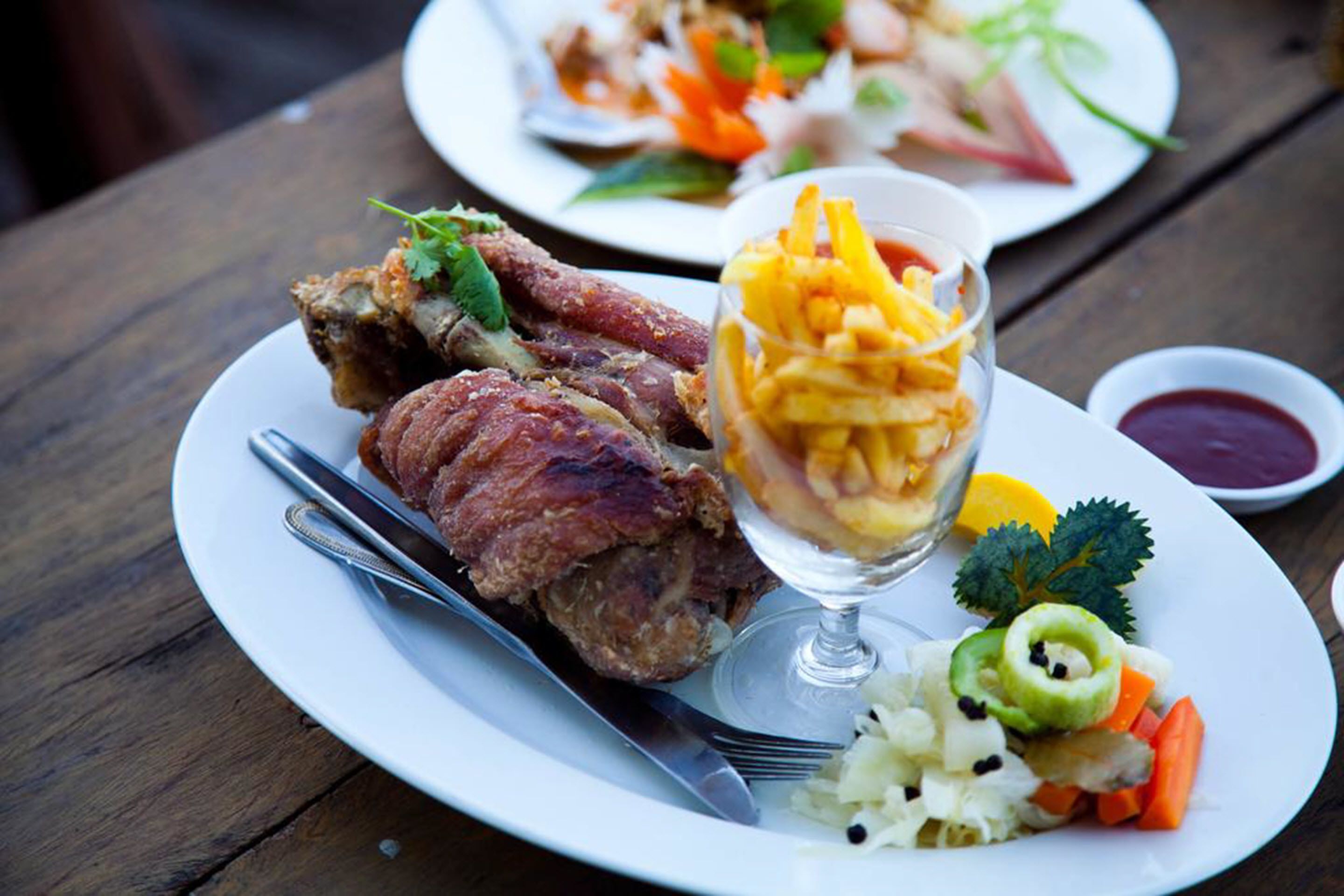 A plate with meat, vegetables, and a glass of sauce.