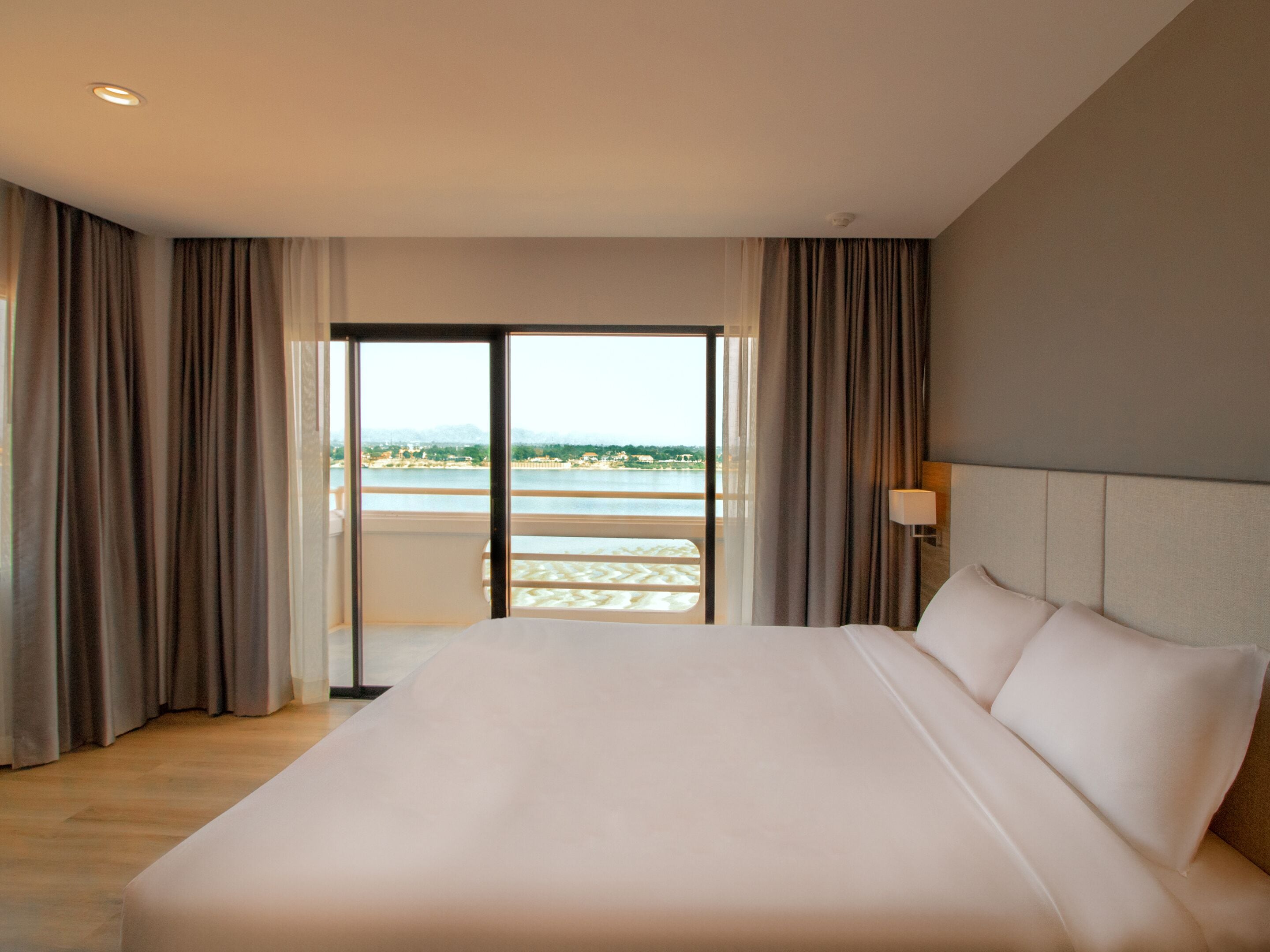 Une chambre d’hôtel avec un grand lit, une vue sur un plan d’eau et un balcon avec des rideaux.