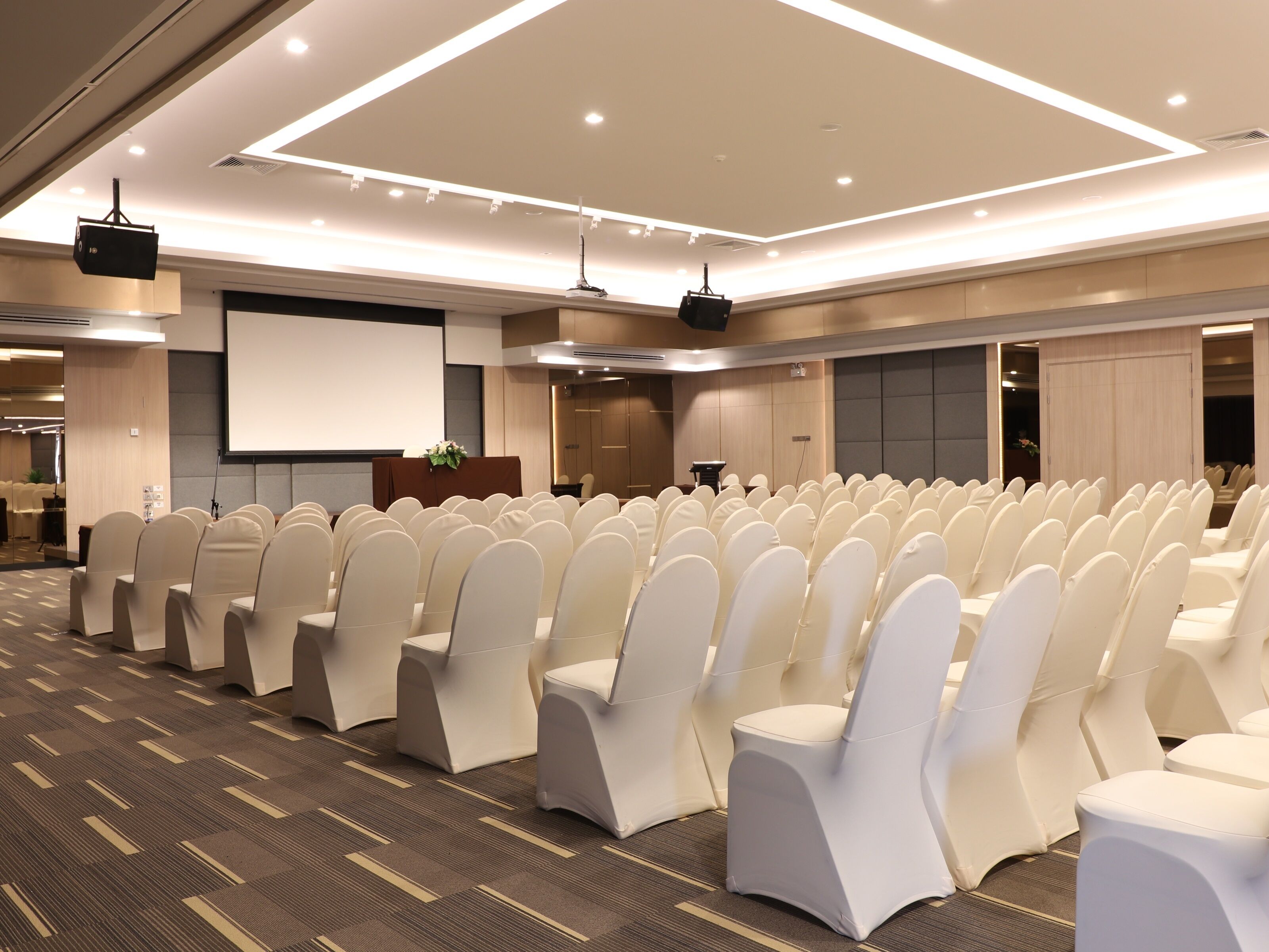 A conference room with rows of white chairs, a projector screen, and a podium.