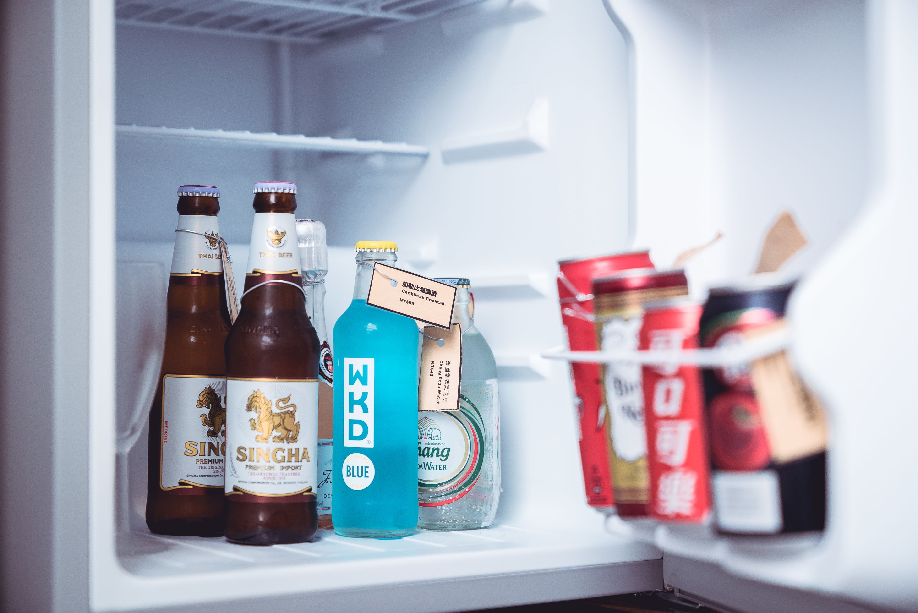 Een koelkast met diverse dranken, waaronder flessen Singha bier, een blauwe fles WKD en een pak water.