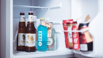 Een koelkast met diverse dranken, waaronder flessen Singha bier, een blauwe fles WKD en een pak water.