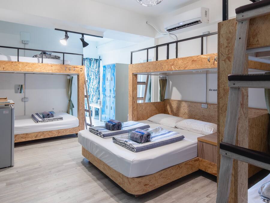 A dormitory room with bunk beds, a small kitchenette, and a window with curtains.