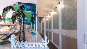 A reception desk with a 'Welcome' sign, a decorative palm tree, and a patterned wall in a hotel lobby. - EATzzZ Hostel (Kaohsiung)