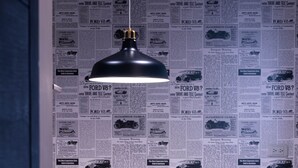 A bedroom with a bed, a bedside table with a plant, and a wall covered with newspaper clippings. - EATzzZ Hostel (Kaohsiung)