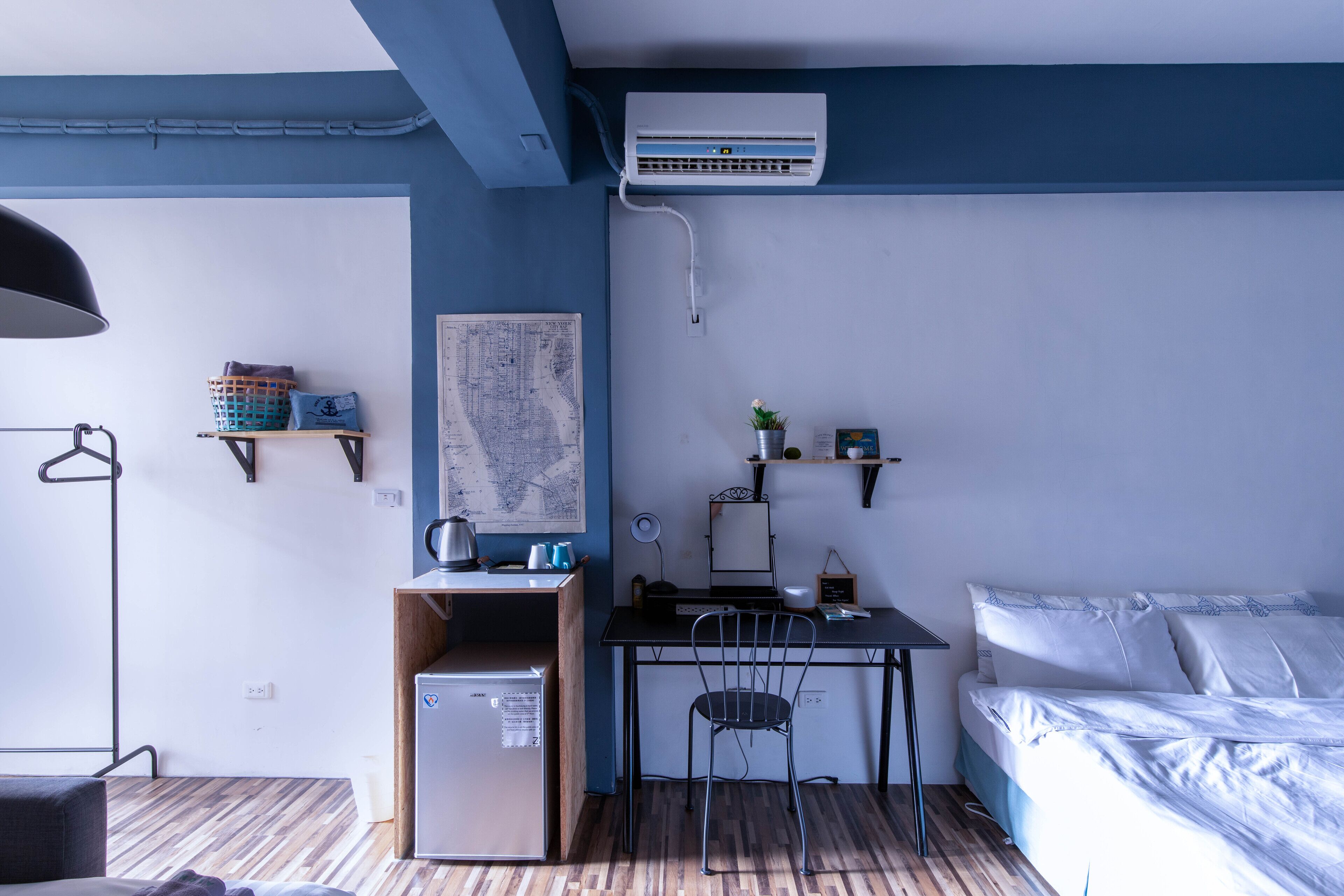 A compact room with a bed, a desk, a chair, a small refrigerator, and a map on the wall.