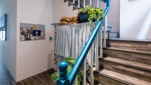 A staircase with a blue handrail, a welcome sign, and a wall with a poster and a plant. - EATzzZ Hostel (Kaohsiung)