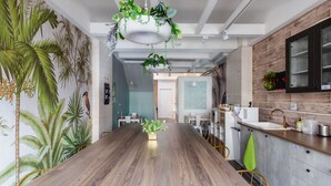 A modern kitchen with a wooden dining table, hanging plants, and a large window. - EATzzZ Hostel (Kaohsiung)