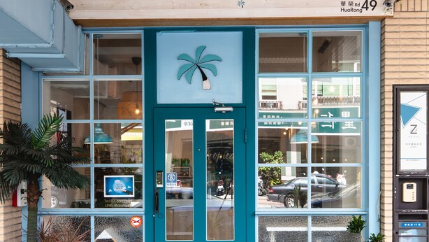 A storefront with a teal door, a palm tree decoration, and several potted plants. - EATzzZ Hostel (Kaohsiung)
