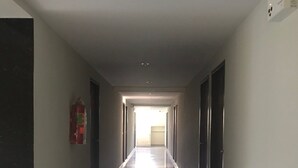 A long, narrow hallway with a shiny tiled floor, a fire extinguisher on the left, and a light fixture on the ceiling.