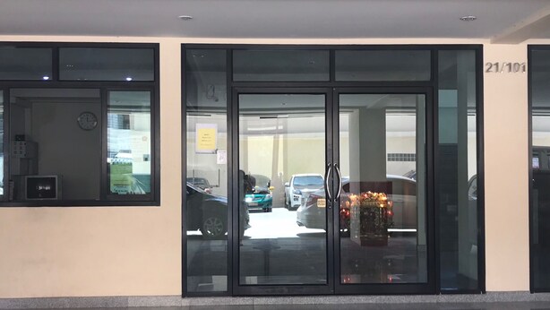 A building entrance with glass doors, a clock, and a parking garage in the background.