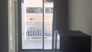 A room with a sliding glass door leading to a balcony, a small refrigerator, and a tiled floor.