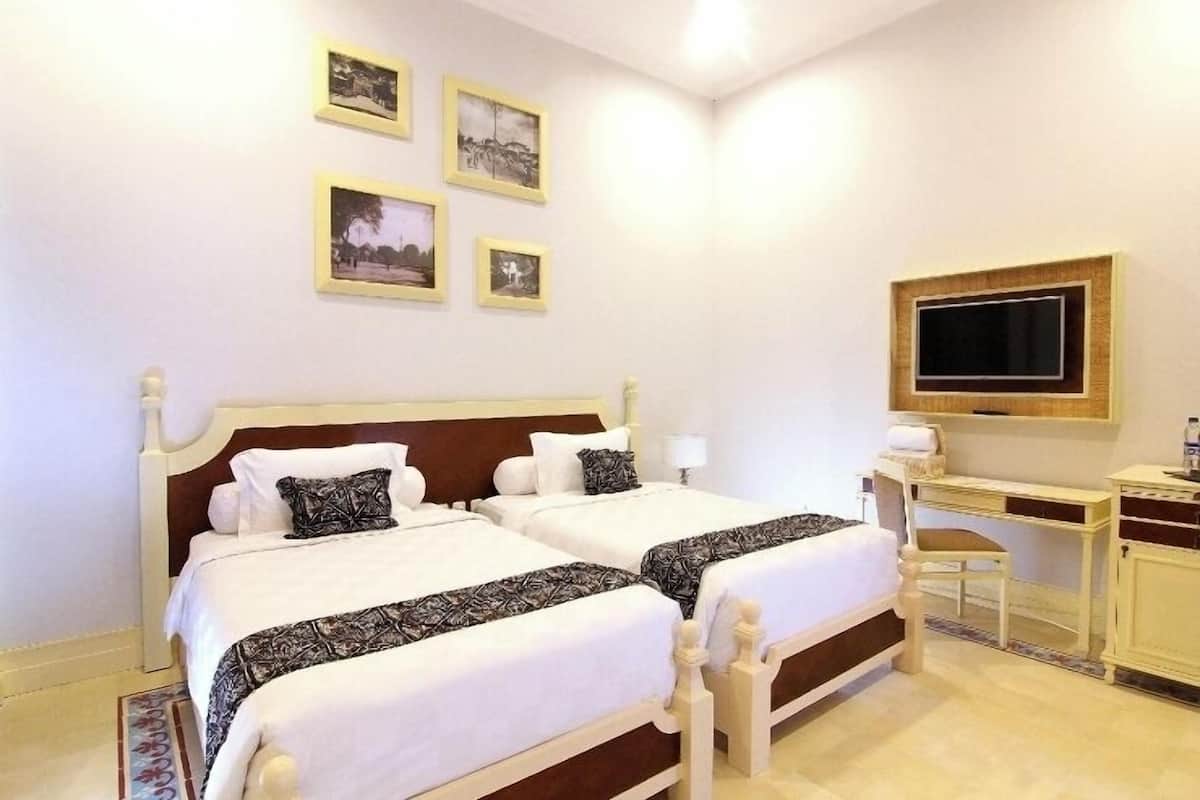 Ett hotellrum med två sängar, ett skrivbord, en stol och en tv på väggen.