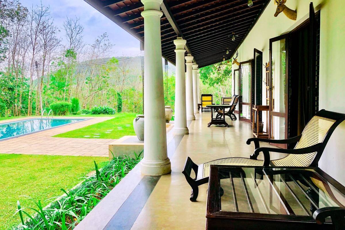 A covered outdoor area with a pool, seating, and a view of the surrounding greenery.