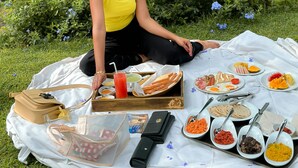 Una persona sentada sobre una manta al aire libre, con una preparación para picnic que incluye comida y una guitarra.
