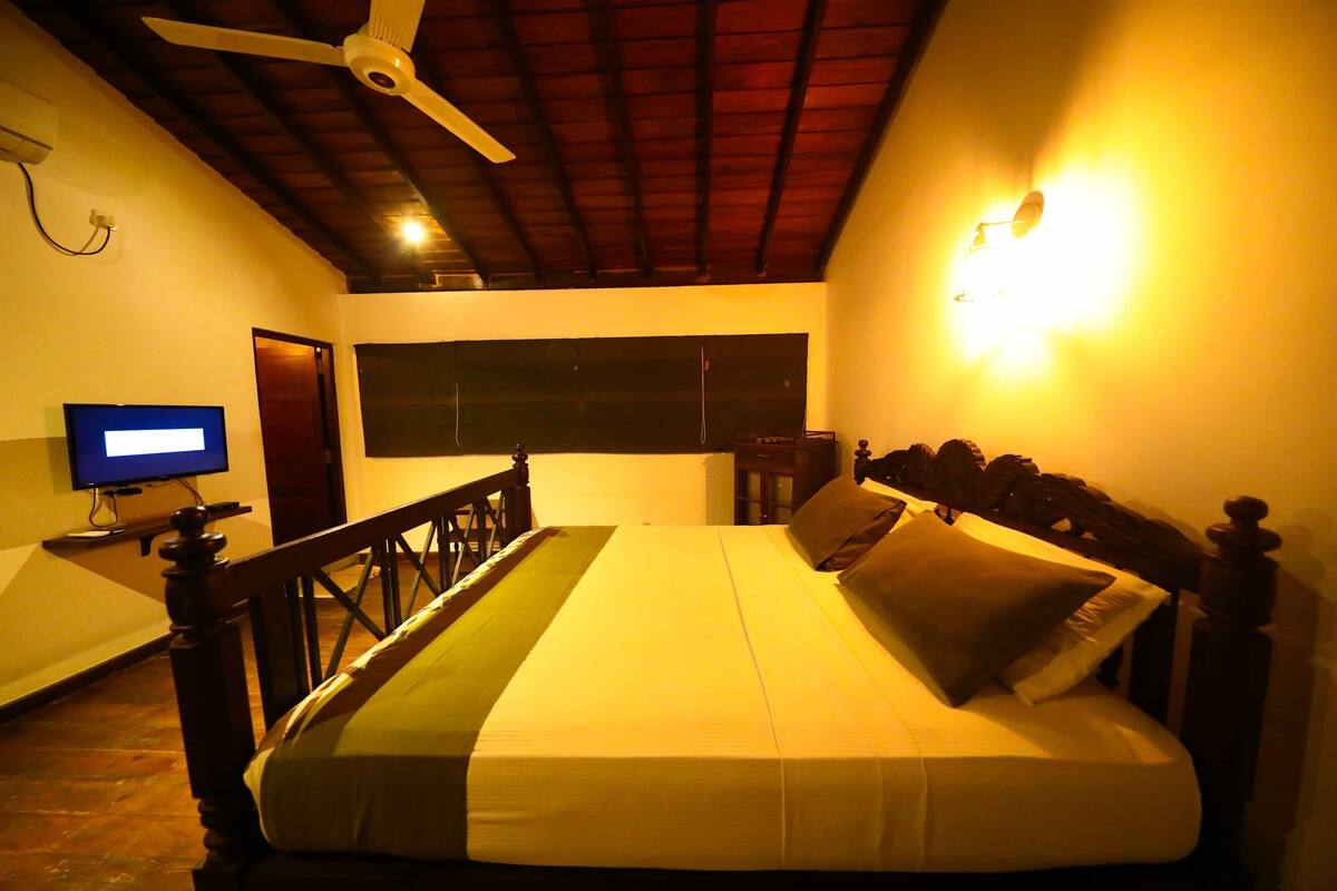 A bedroom with a bed, a ceiling fan, a television, and a wall-mounted light fixture.