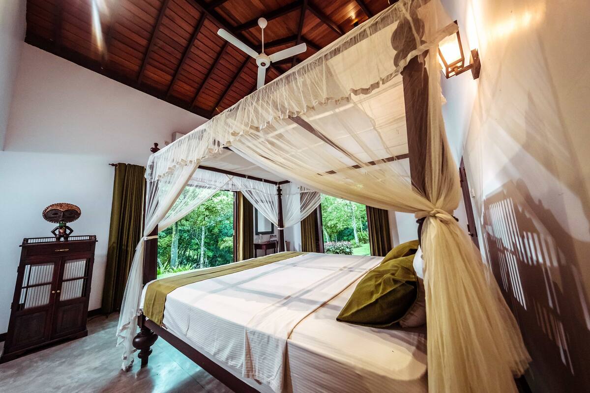 A room with a bed under a canopy, a wooden cabinet, and a window with curtains.