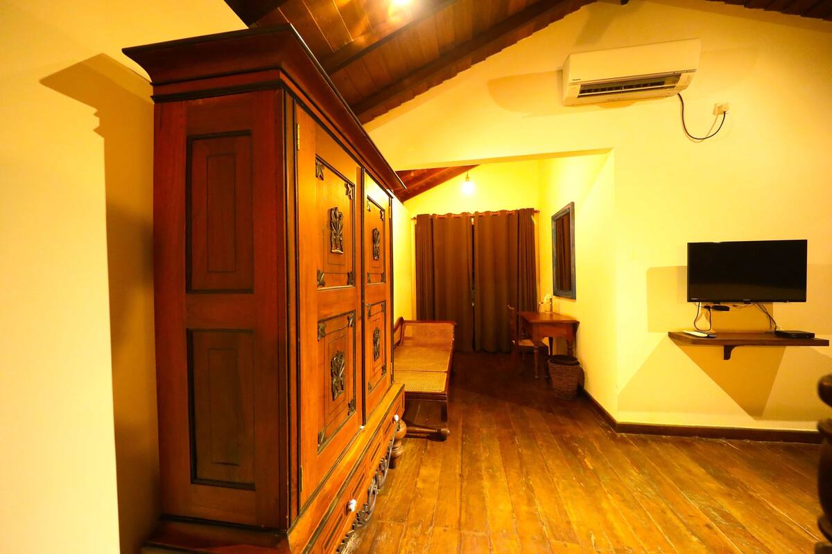 A room with wooden flooring, a large wooden cabinet, a television, and a ceiling fan.