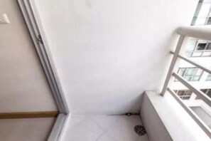 A narrow balcony with a white railing, a tiled floor, and a view of other buildings.