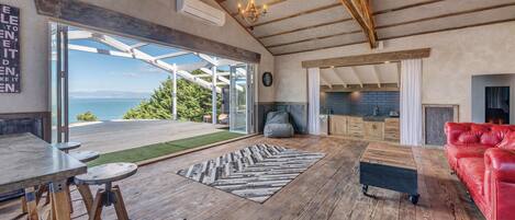 A spacious living area with a wooden floor, a red leather sofa, a fireplace, and a large window offering a view of the outdoors.