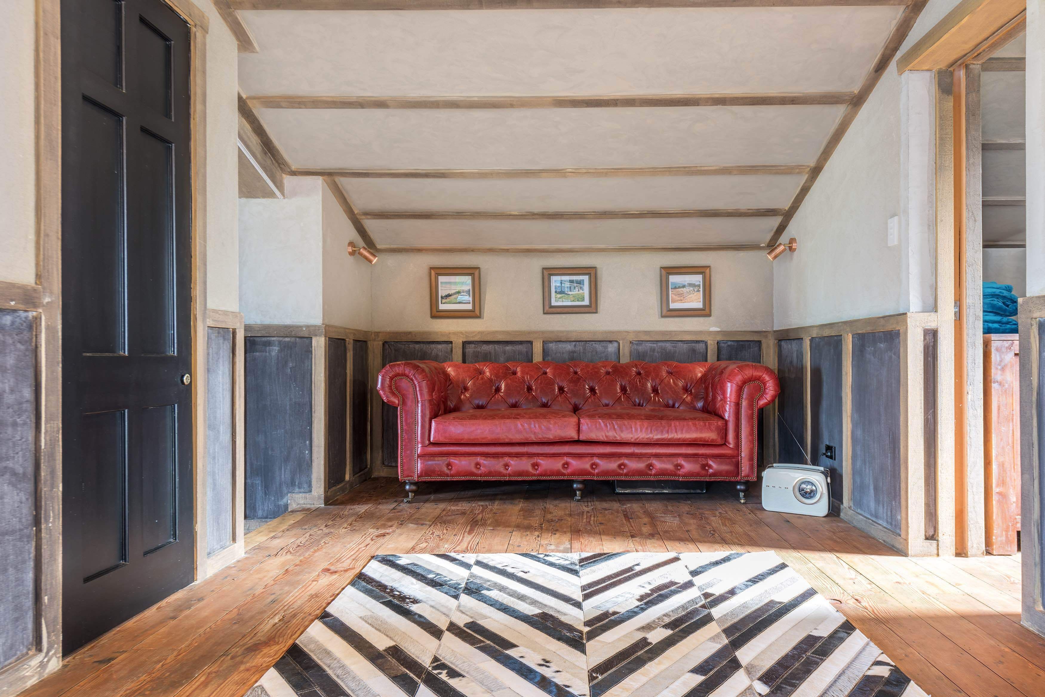 A room with a red leather sofa, wooden flooring, and a patterned rug.