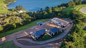 An aerial view of a coastal property with a large house, a swimming pool, and a view of the sea. - Woodside Bay Chalets (Waiheke Island)