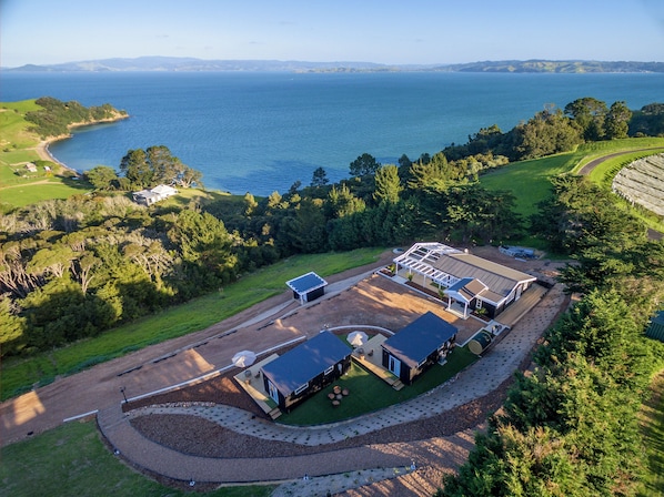 An aerial view of a coastal property with a large house, a swimming pool, and a view of the sea. - Woodside Bay Chalets (Waiheke Island)