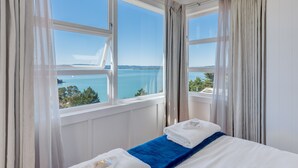 A hotel room with a bed, a view of the sea, and a window with curtains. - Woodside Bay Chalets (Waiheke Island)