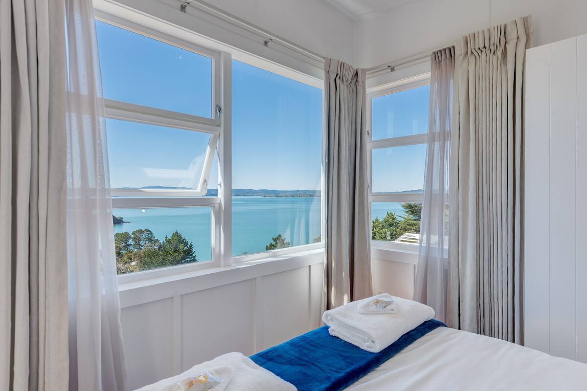 A hotel room with a bed, a view of the sea, and a window with curtains.