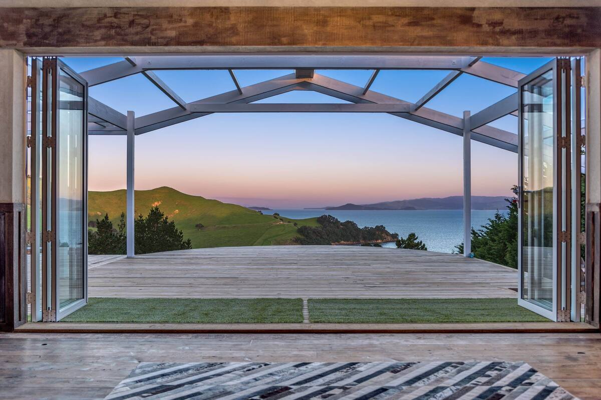 An open wooden deck with glass doors leading to a scenic view of hills and a body of water.