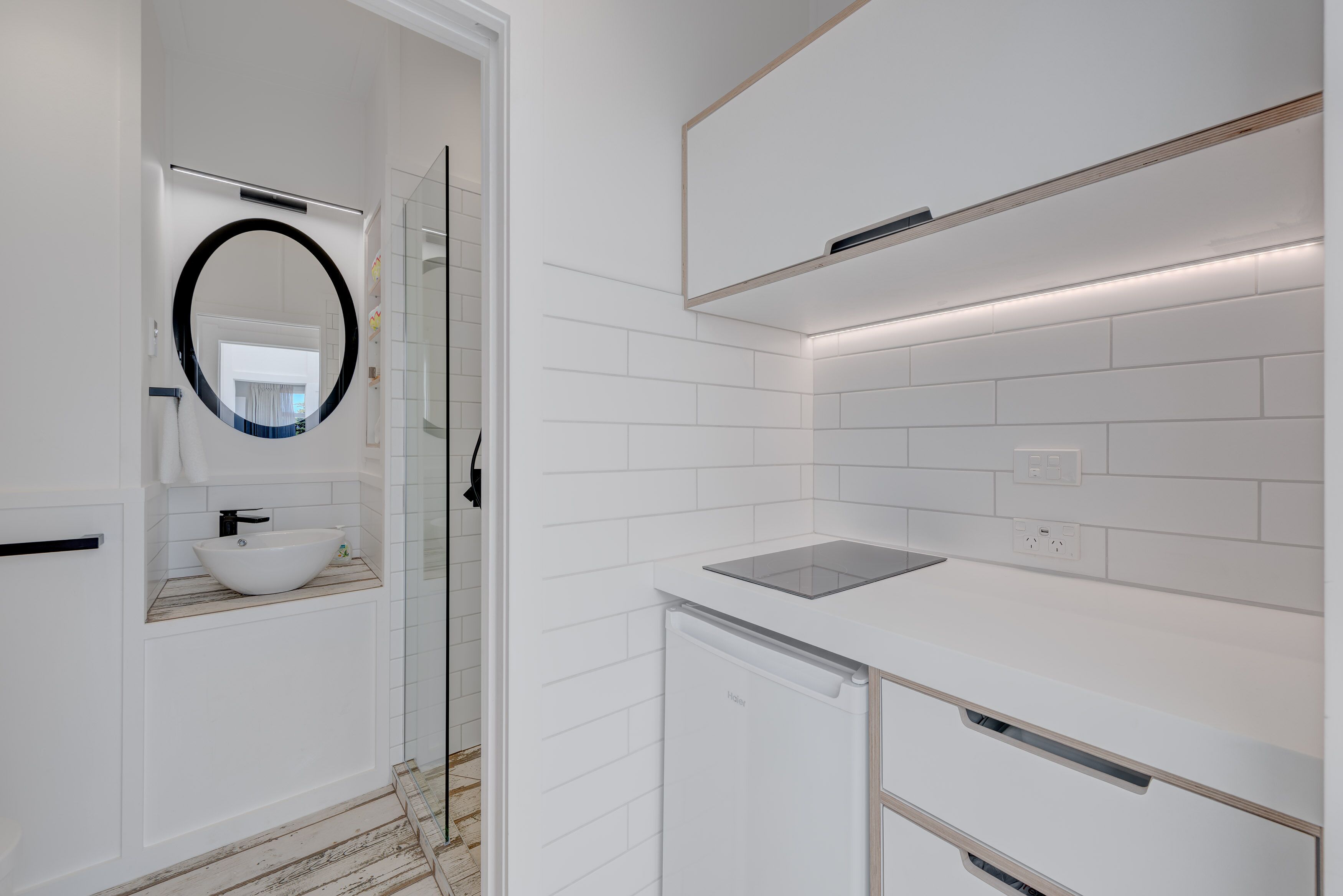 A modern bathroom with a white sink, a round mirror, and a glass shower enclosure.