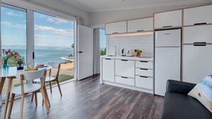 A modern kitchen with white cabinets and a large window overlooking the sea. - Woodside Bay Chalets (Waiheke Island)