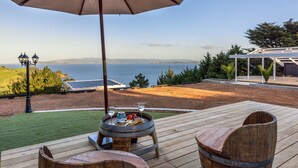 A wooden deck with a table and chairs, a barrel, and a large umbrella. - Woodside Bay Chalets (Waiheke Island)
