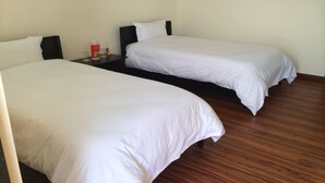 Two single beds with white linens in a room with wooden flooring and a plain wall. - Nepal Yoga Retreat (Changunarayan)