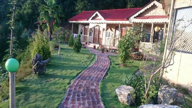 A house with a brick pathway leading to a porch, surrounded by greenery and rocks. - Nepal Yoga Retreat (Changunarayan)