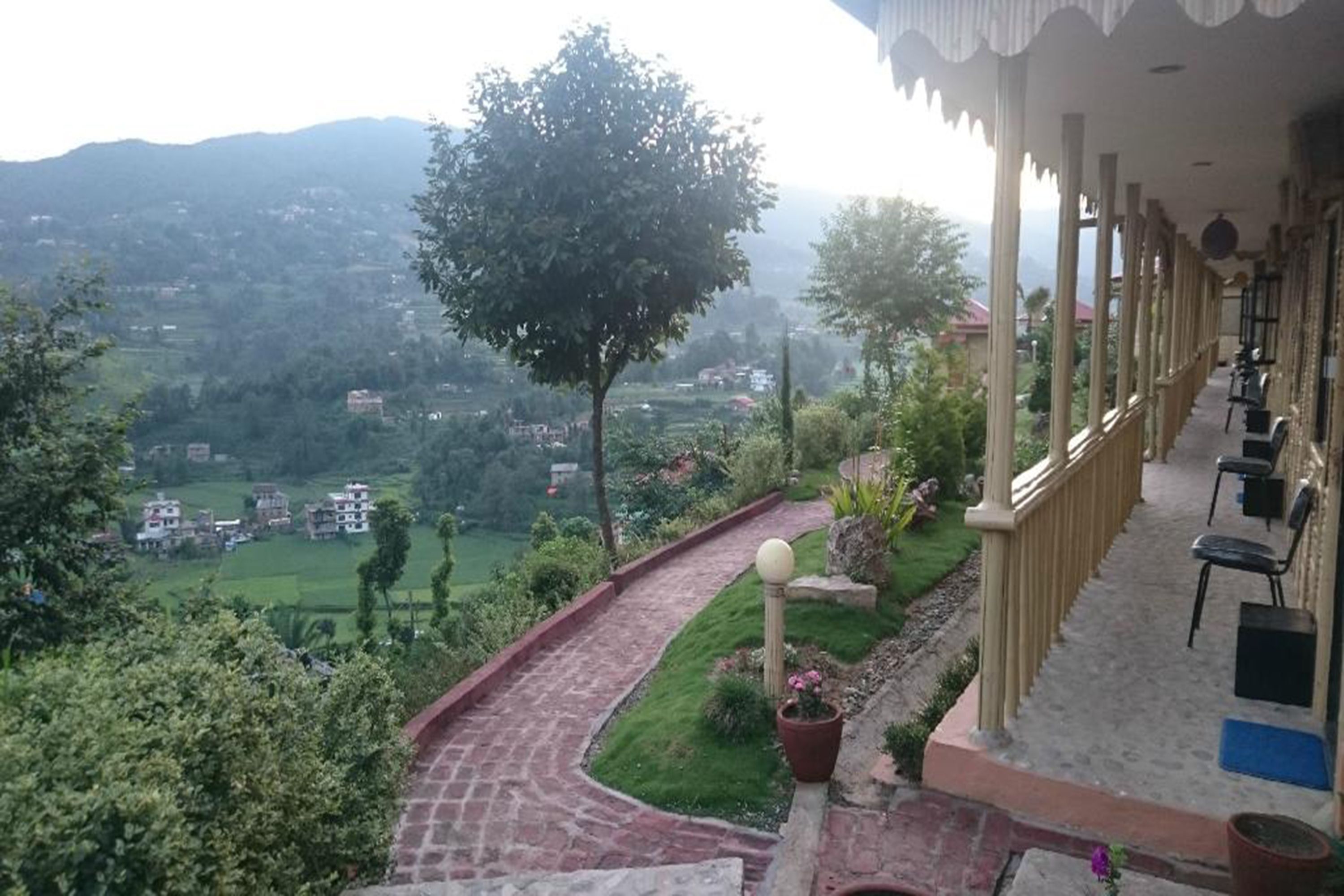 Un hotel con una zona de estar al aire libre techada, un sendero pavimentado y vistas del paisaje circundante.