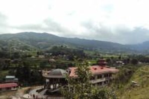 A mountainous landscape with a building featuring a red roof and a dome structure. - Nepal Yoga Retreat (Changunarayan)