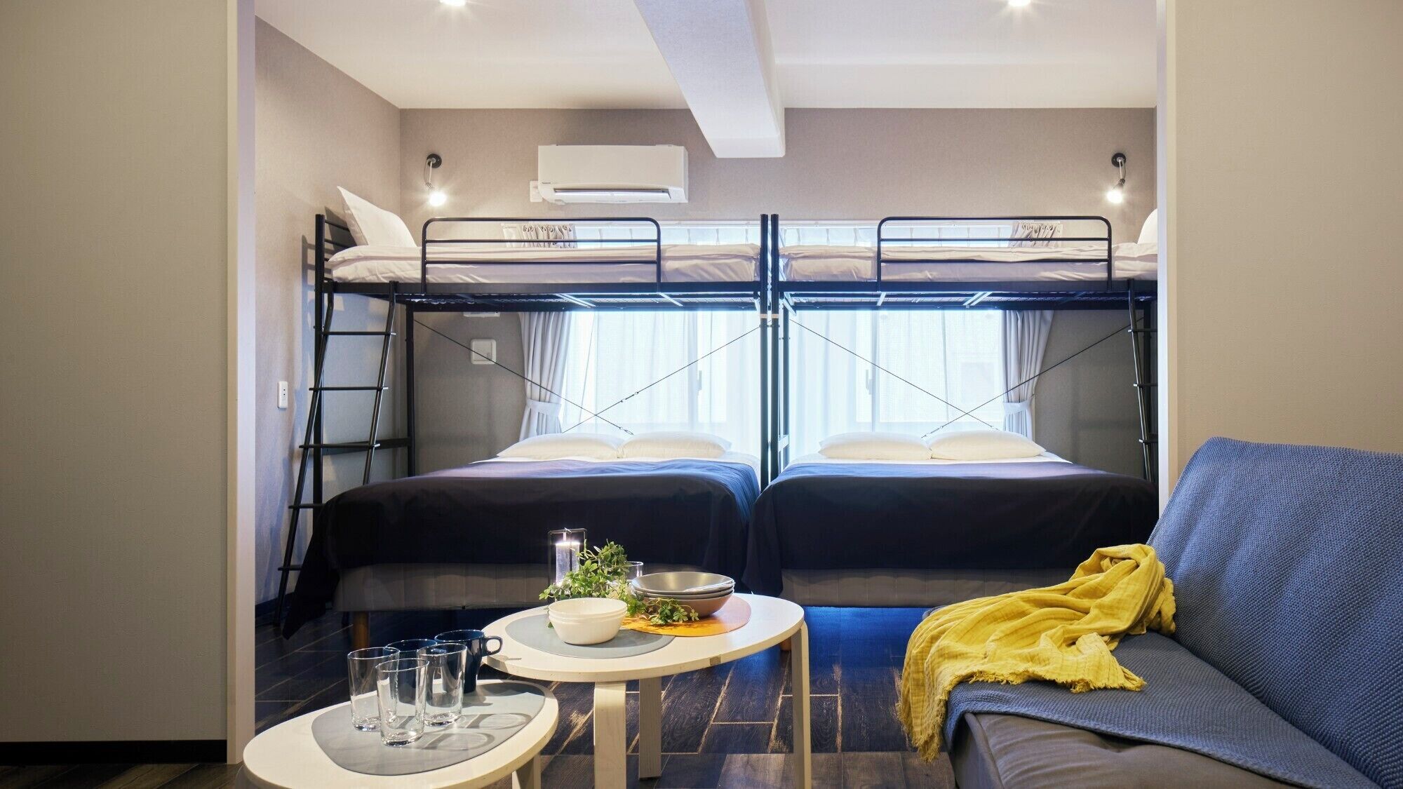 Une pièce compacte avec des lits superposés, un canapé, une petite table avec un saladier et des verres, et une fenêtre avec des rideaux.